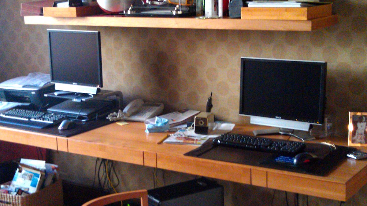 Handcrafted built-in wooden desk with integrated wall shelving and extended work surface designed as a custom multi-station workspace.