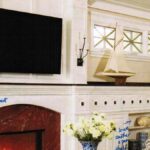 Handcrafted white fireplace mantel with integrated media wall, built-in open shelving, extended mantel shelf, and wall-mounted TV in a living room.