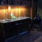 Built-in outdoor kitchen prep station with sink, stone countertop, and dark wood cabinetry.