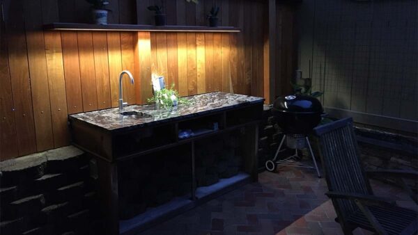 Built-in outdoor kitchen prep station with sink, stone countertop, and dark wood cabinetry.