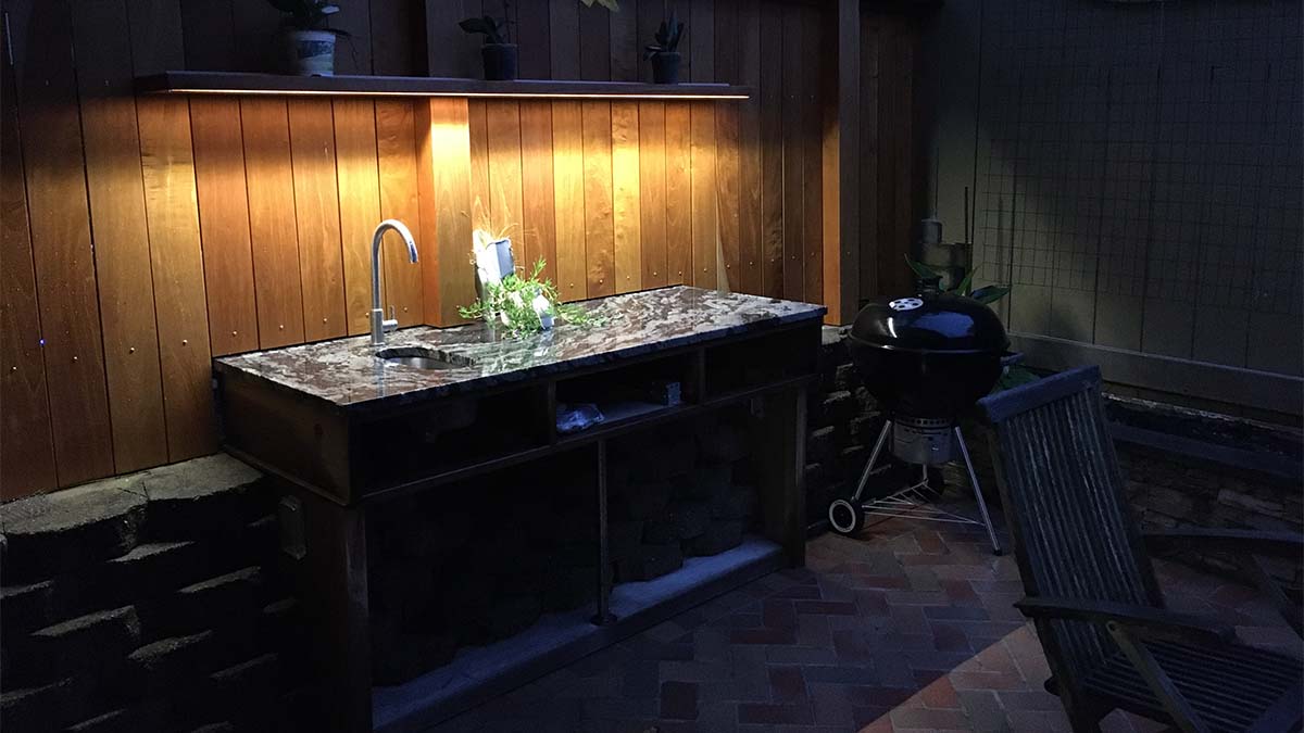 Built-in outdoor kitchen prep station with sink, stone countertop, and dark wood cabinetry.