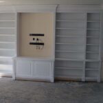 Handcrafted built-in wall shelving unit with white finish, open shelves, and integrated lower cabinetry designed for a living room interior.