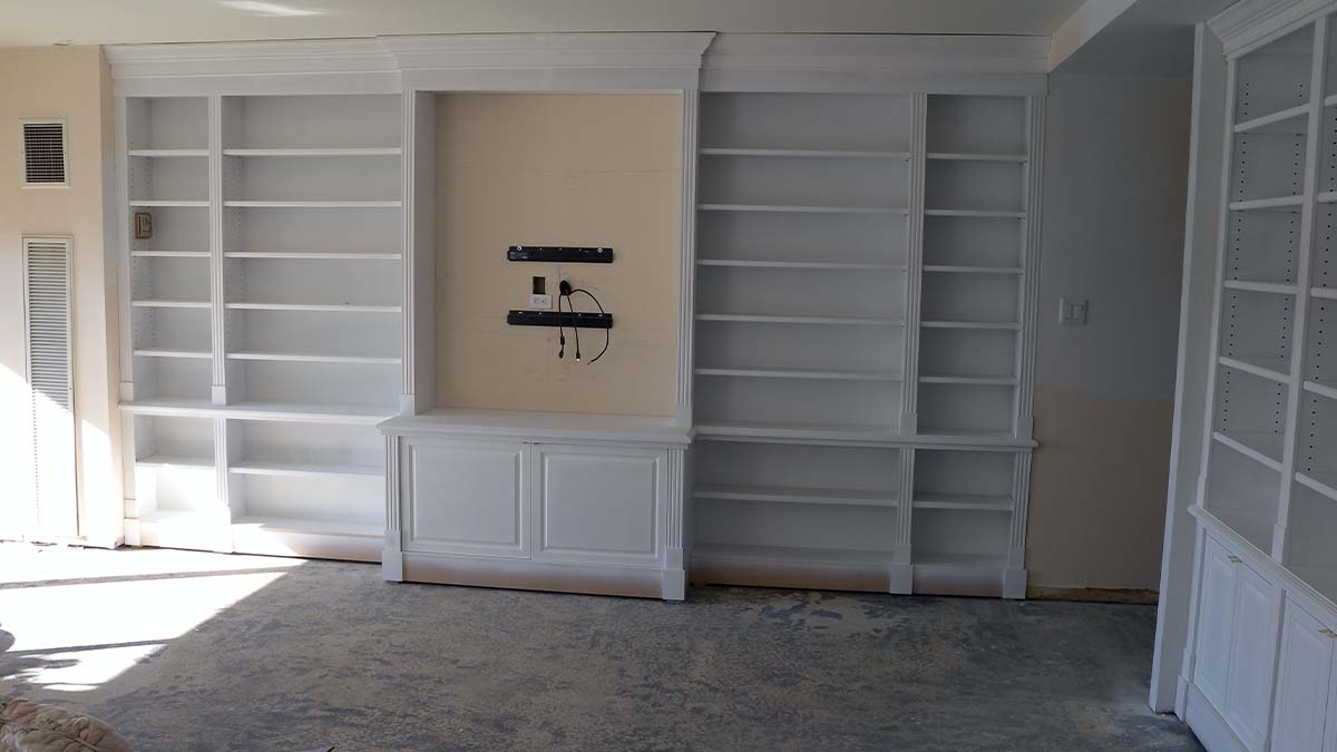 Handcrafted built-in wall shelving unit with white finish, open shelves, and integrated lower cabinetry designed for a living room interior.