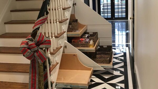 Handcrafted under-stair pull-out storage with white built-in drawers and concealed compartments designed to maximize space beneath a staircase.